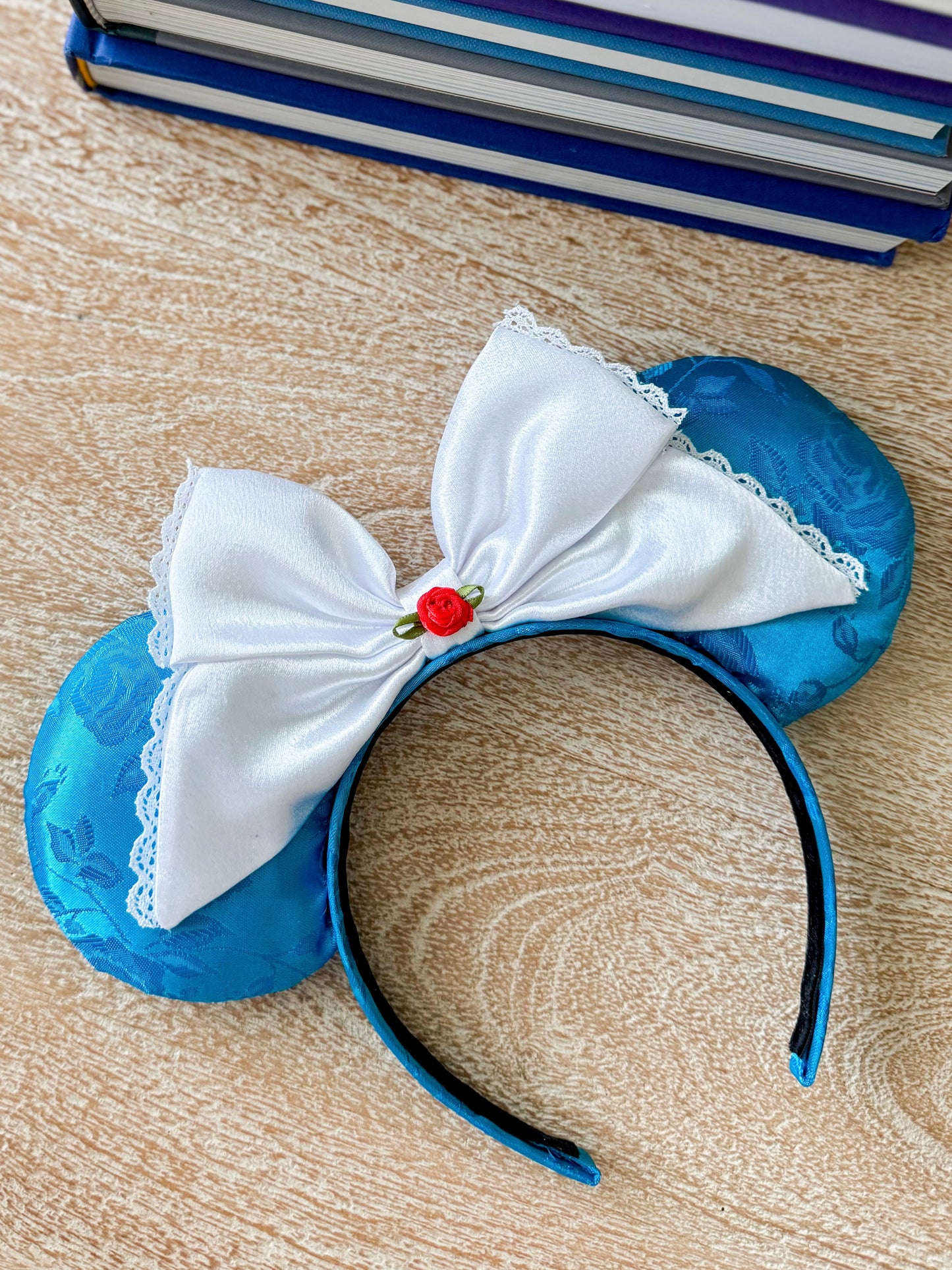 Blue mouse ears with white bow on a wooden surface with books in the corner