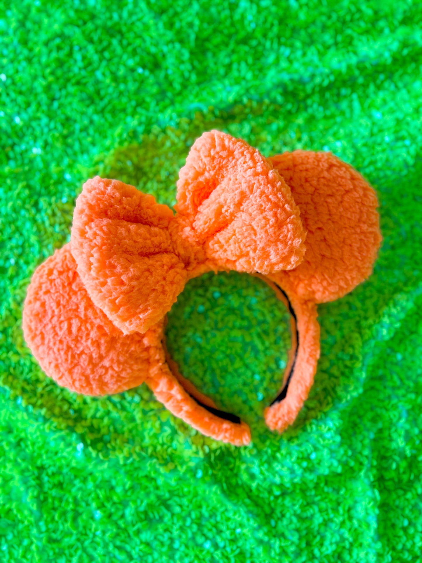 A pair of orange sherpa ears with a bow, placed on a green surface.