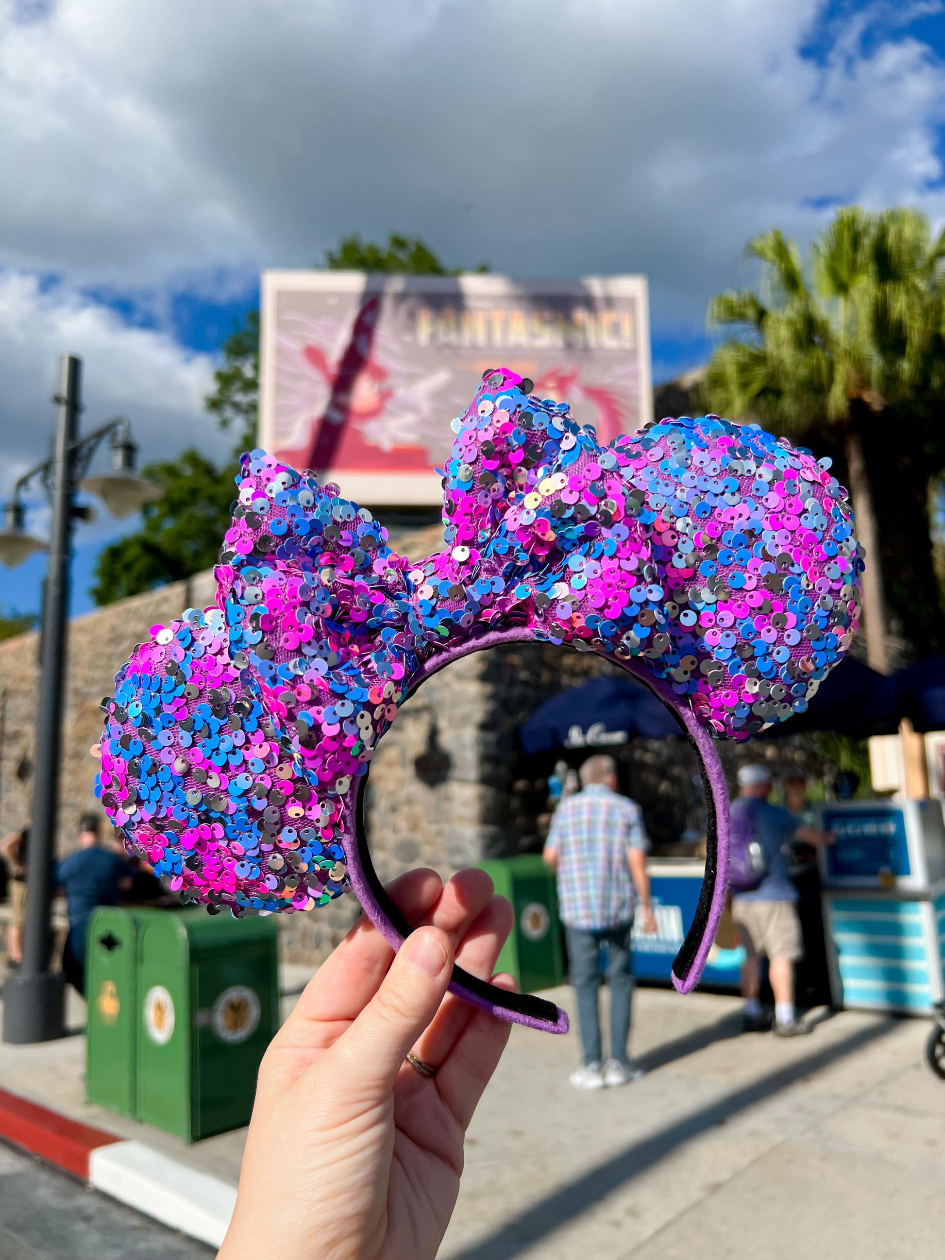A hand holding purple, blue, and silver sequin mouse ears in Hollywood Studios.