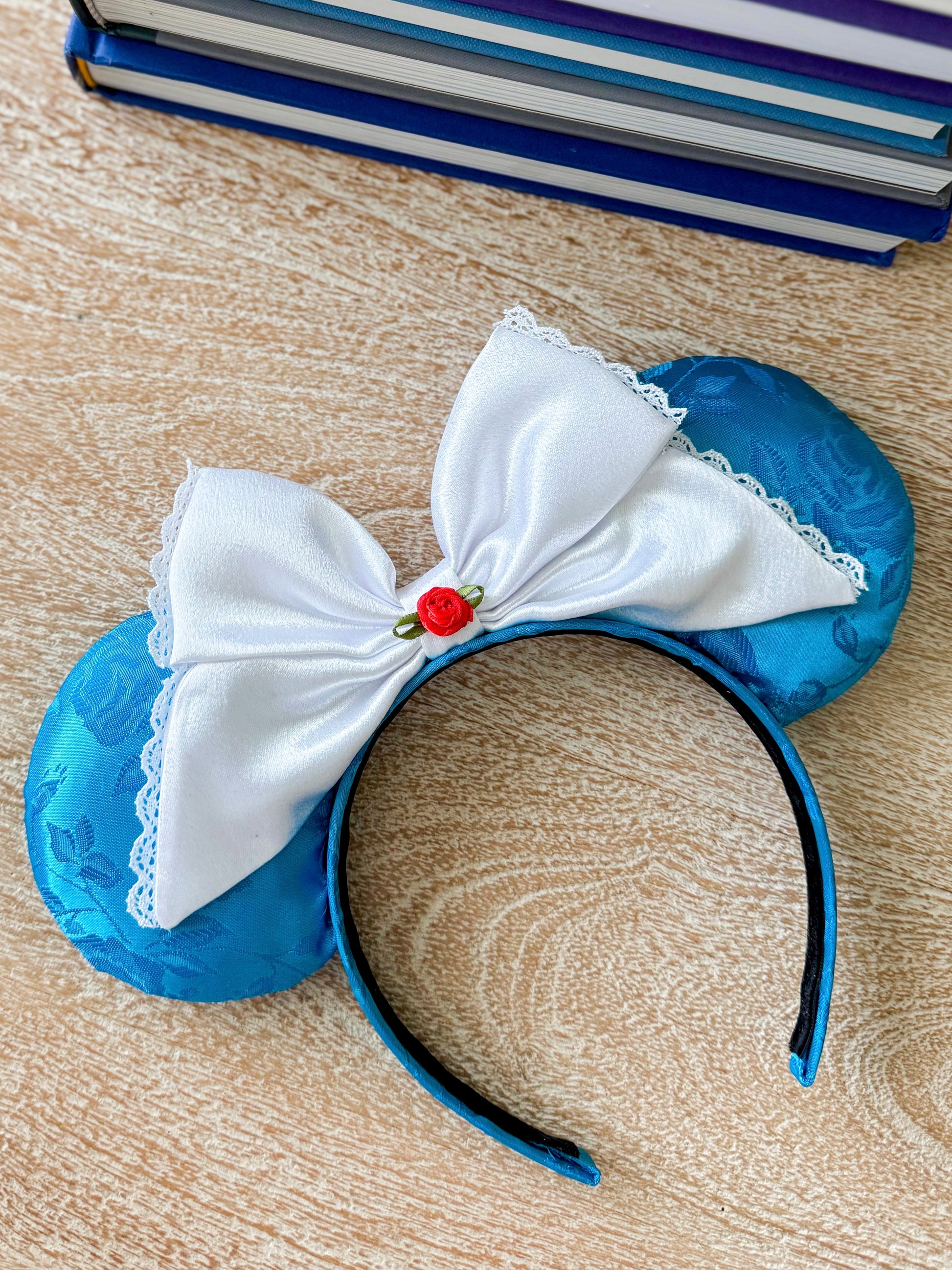 Blue mouse ears with white bow on a wooden surface with books in the corner