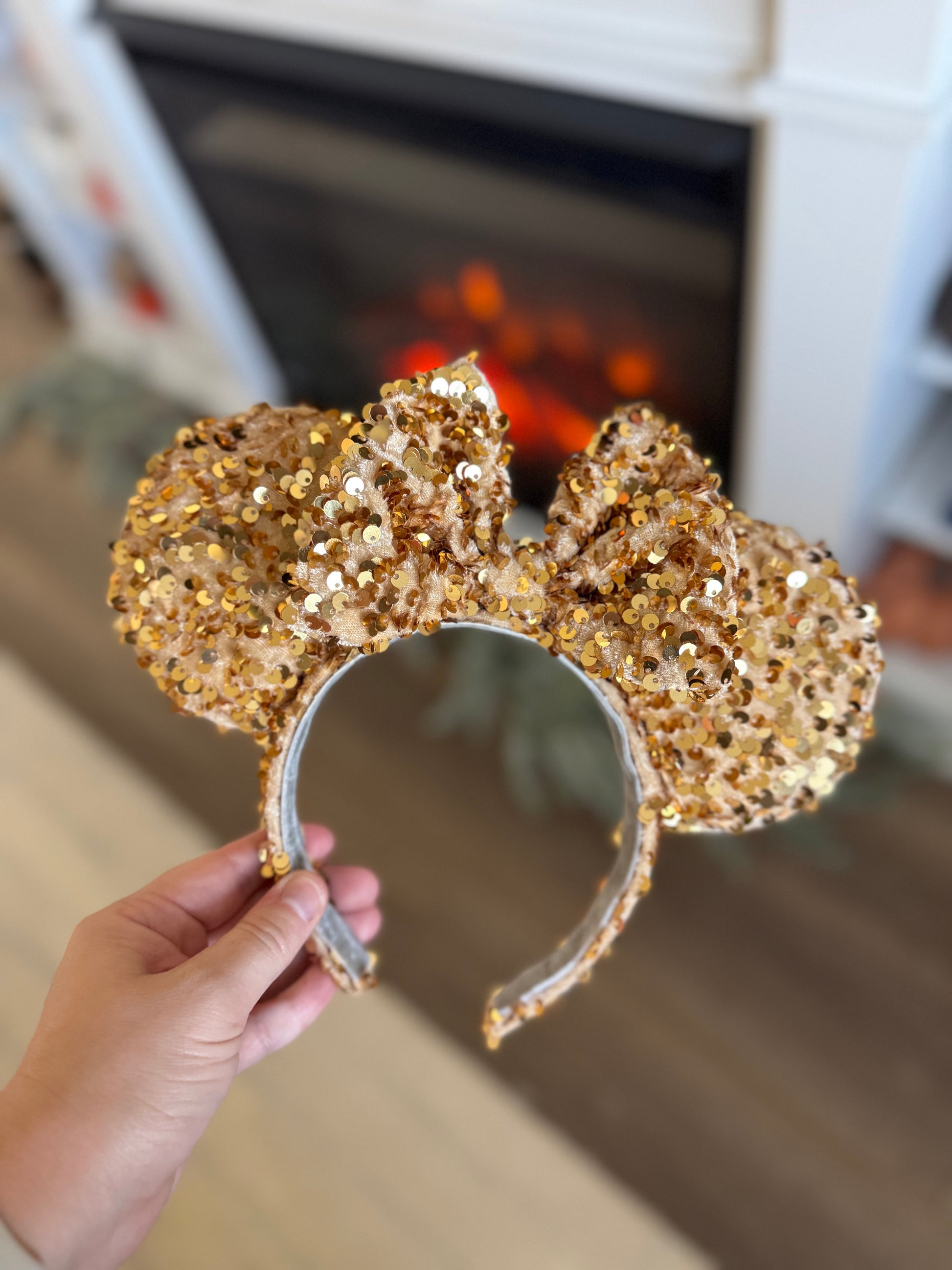 Gold glittery mouse ears held in front of a fireplace.