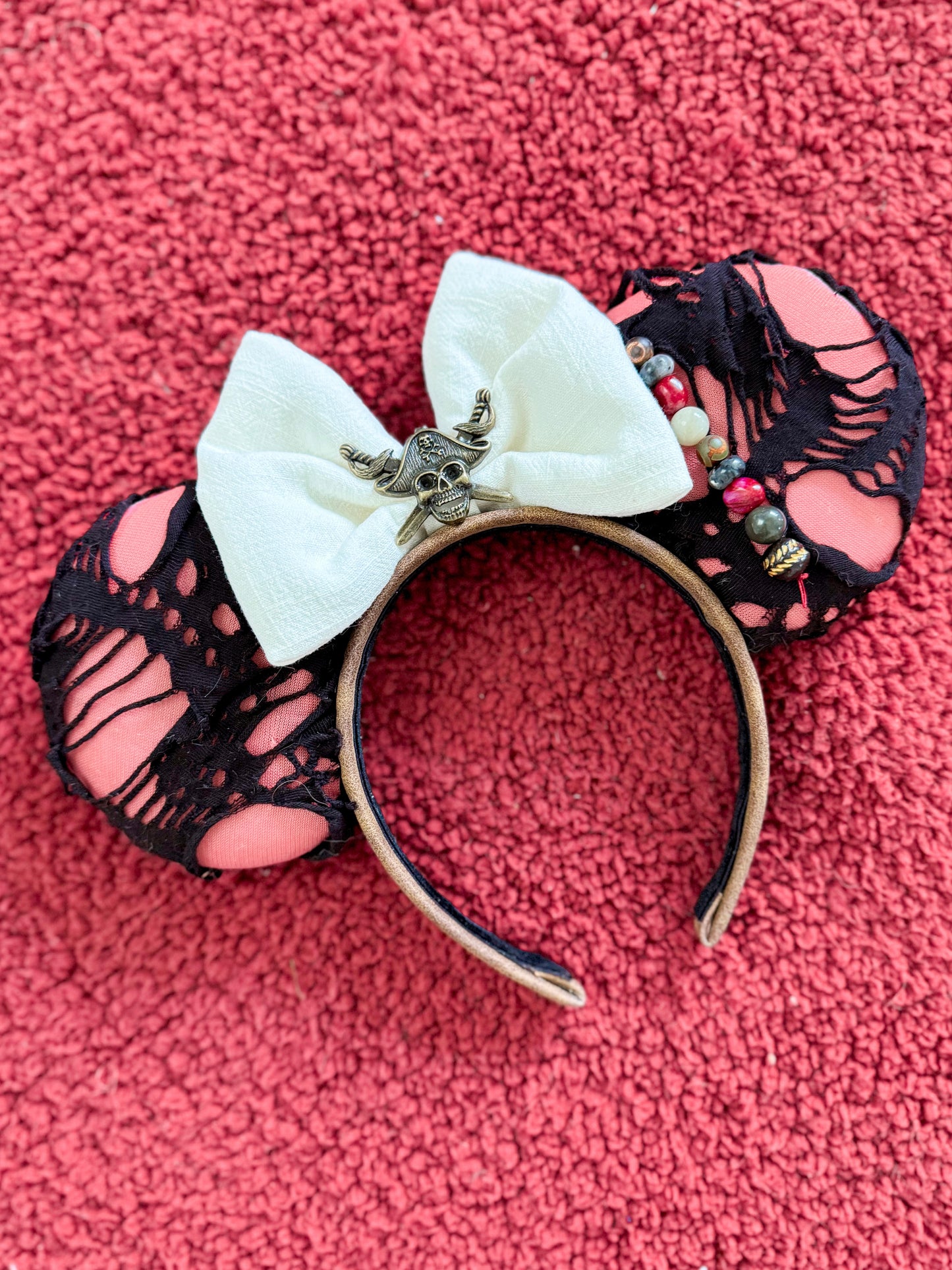 Black ripped fabric with a faded red background with a white bow and skull detail on the bow and beads on the right hand side of the bow