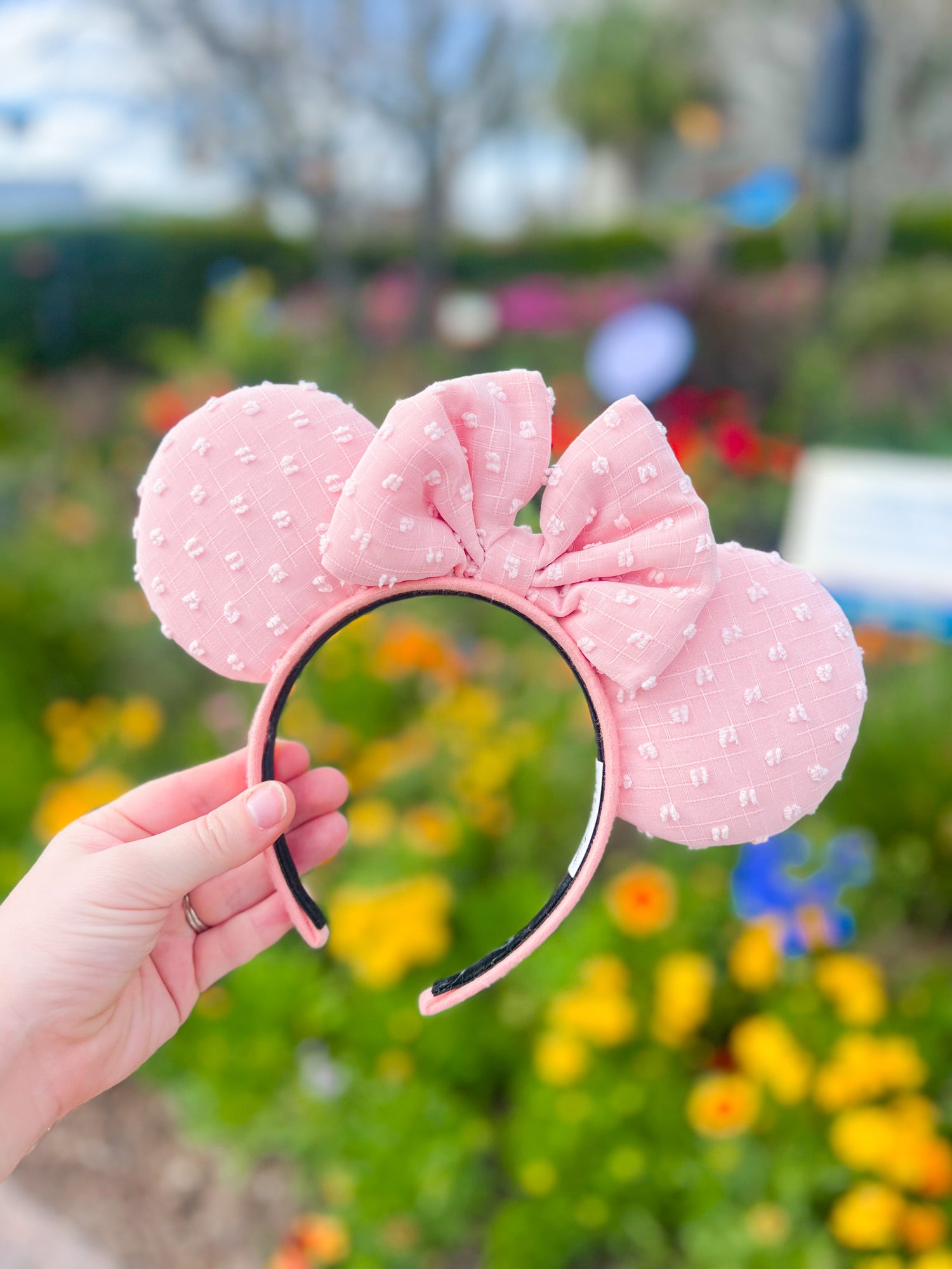 A pink/peach pair of mouse ears with swiss dots displayed in front of a floral background.