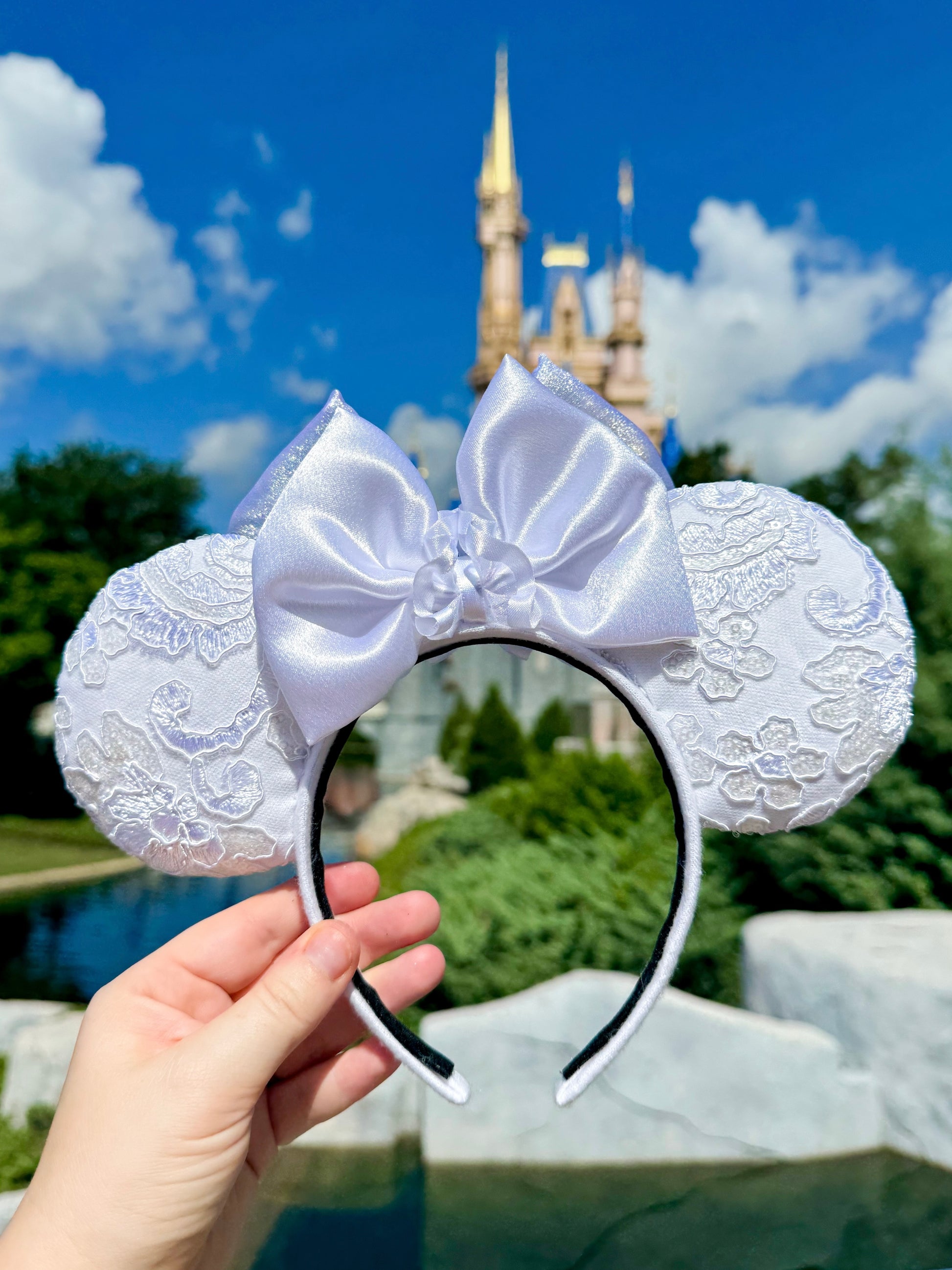 White lace mouse ears with a large bow held in front of Cinderella Castle.