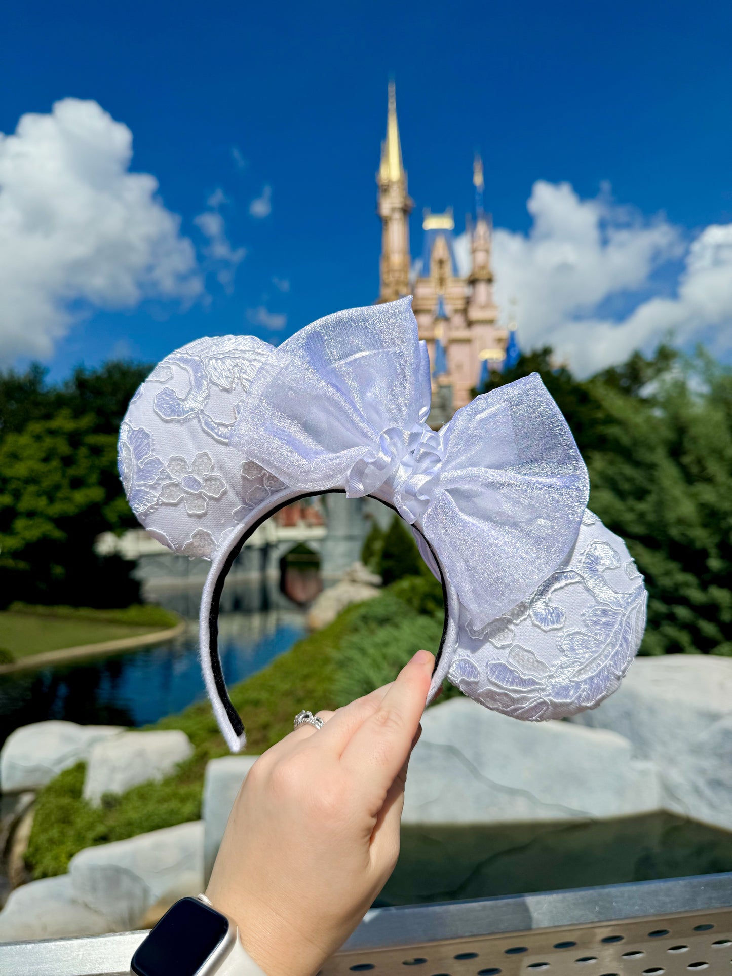 White lace mouse ears held up with a castle in the background (this is the back of the ears from the previous photo)