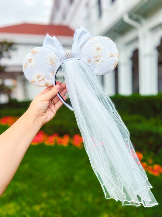 A hand holding a pair of white bridal veil ears attached to a short, rhinestone-studded veil.