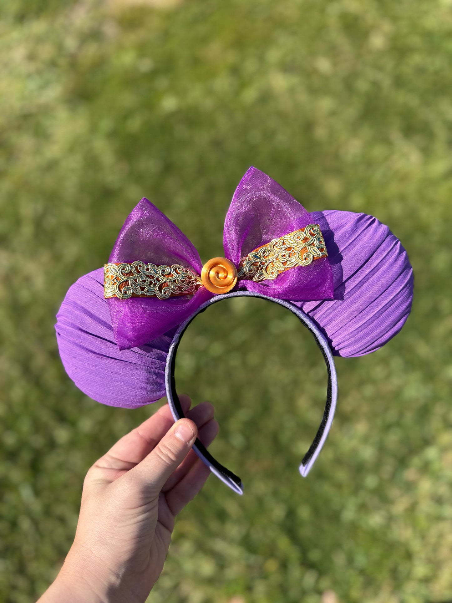 Purple mouse ears with decorative elements held against a grassy background