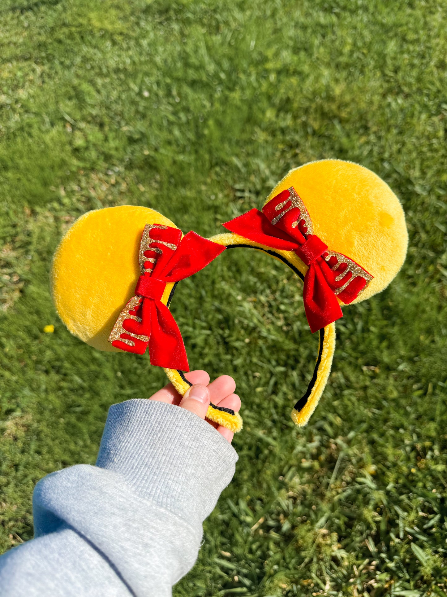 Yellow mouse ears with red bows held against a grassy background
