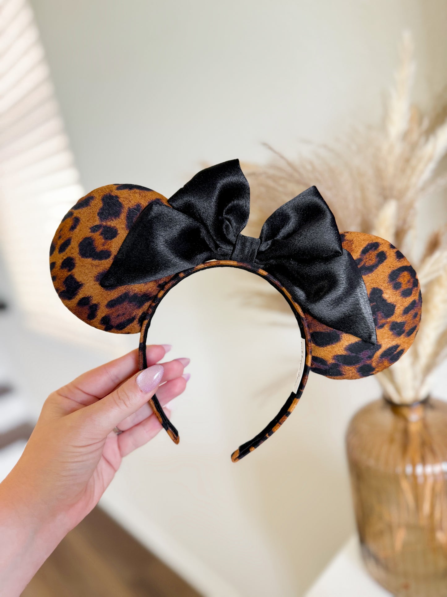 Leopard print headband with a black bow held by a hand against a neutral background