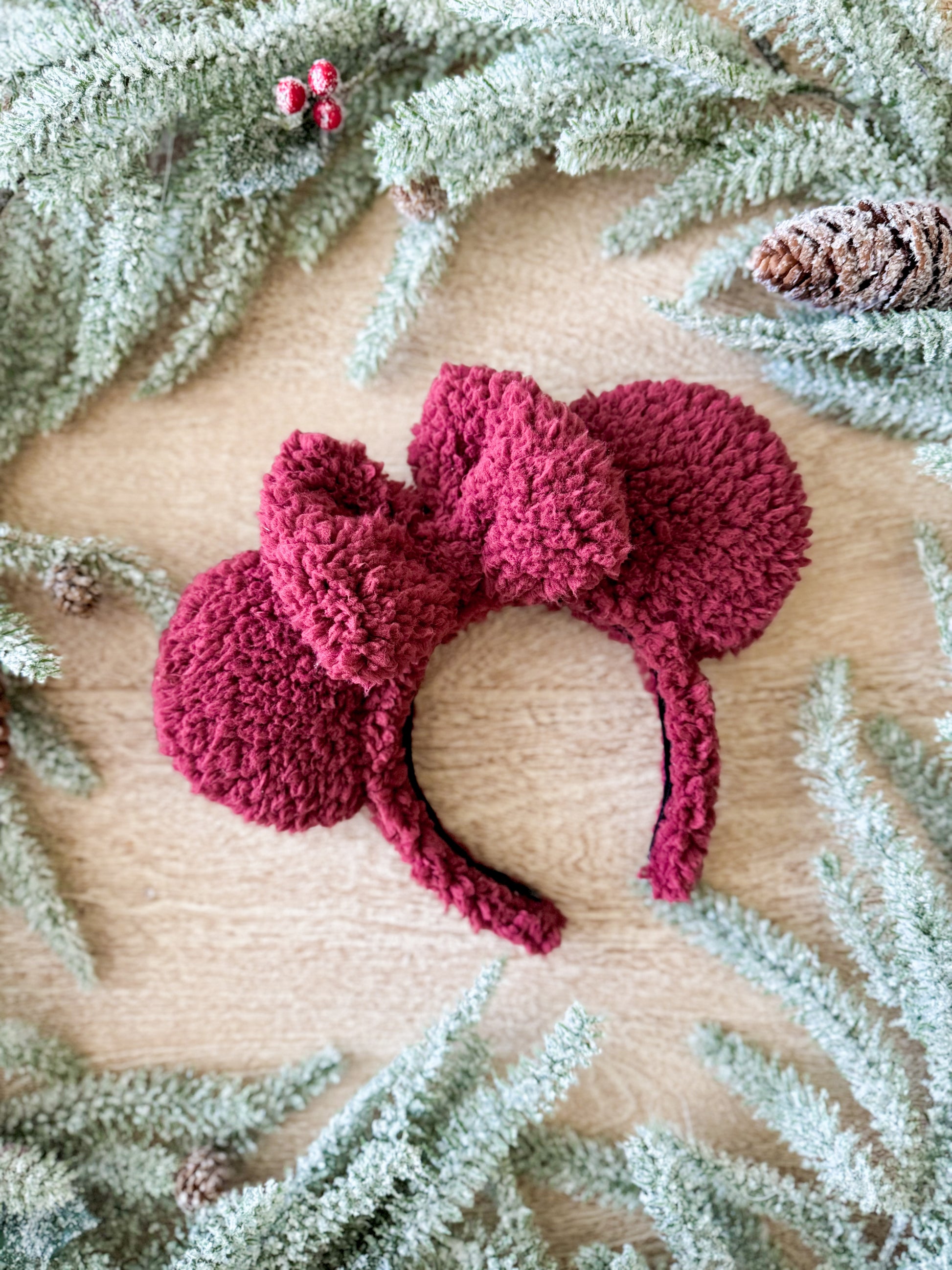 deep red sherpa mouse ears on a wooden surface with greenery