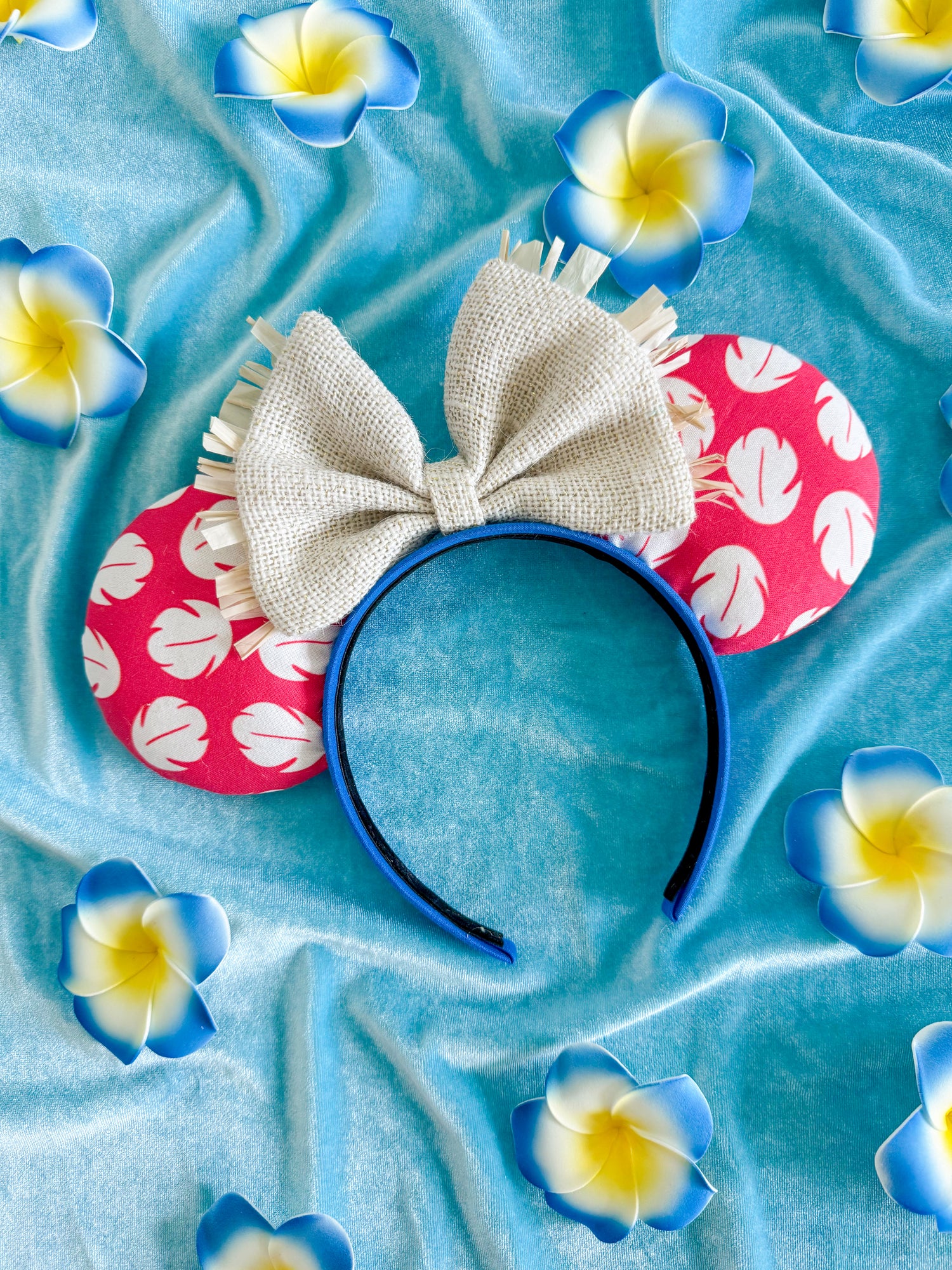 red and white tropical mouse ears with a burlap bow and on a blue textured background with tropical flowers.