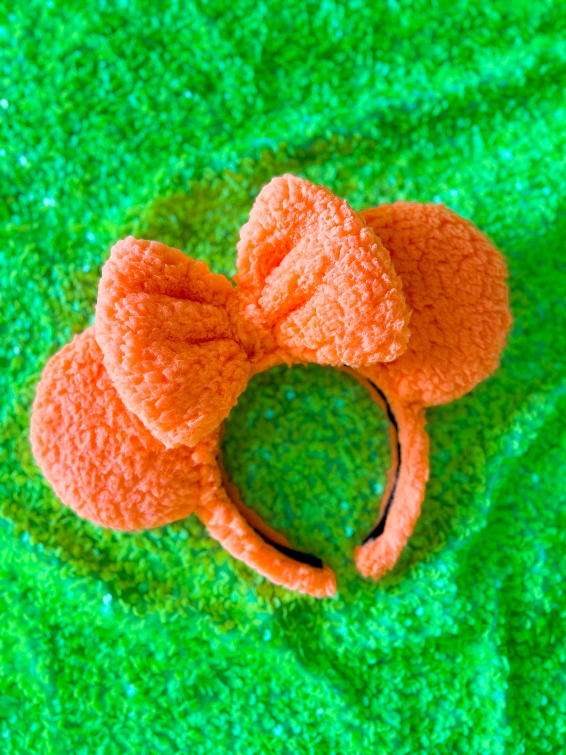 A pair of orange sherpa ears with a bow, placed on a green surface.