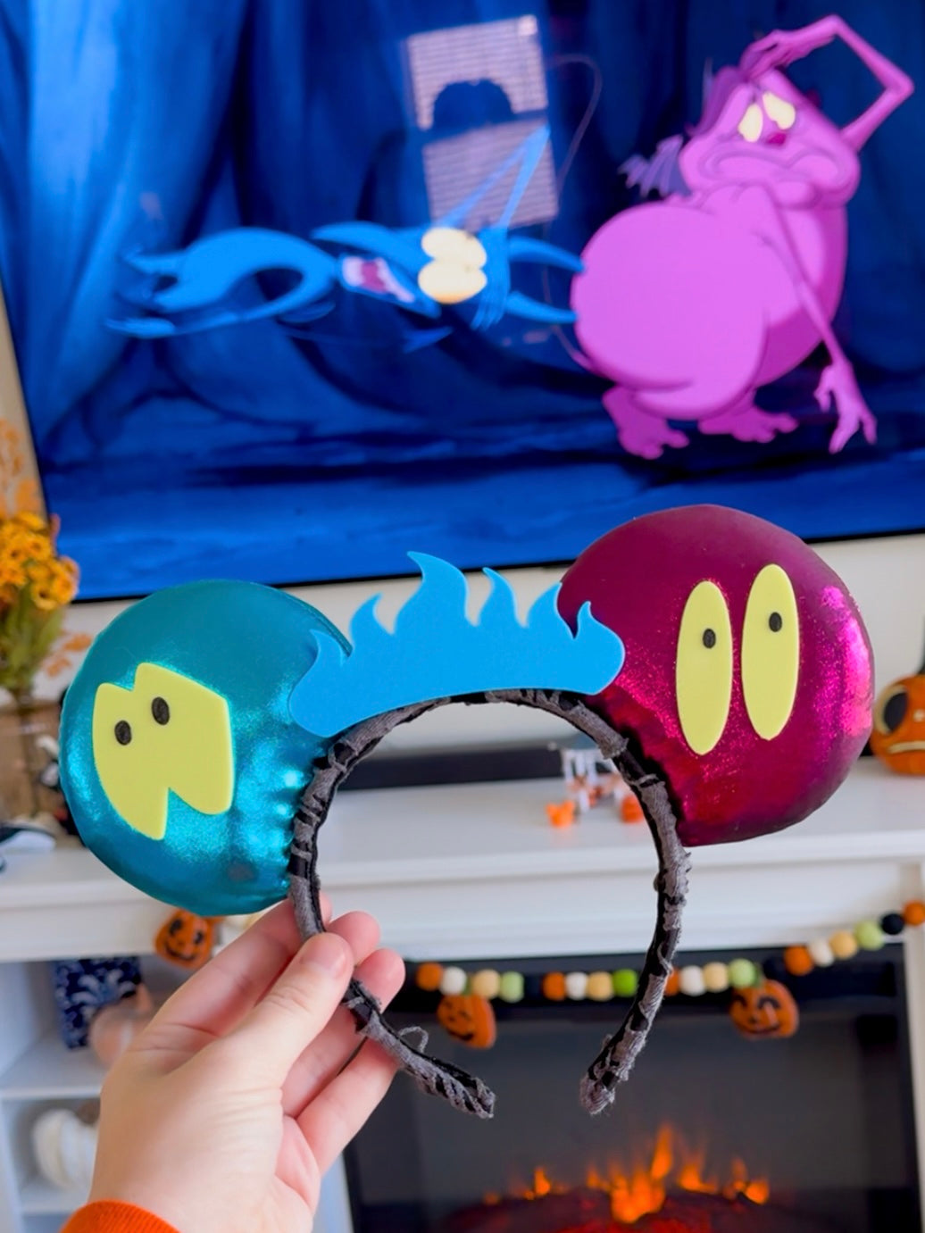 Mouse ears with cartoon character designs held in front of a decorated fireplace.