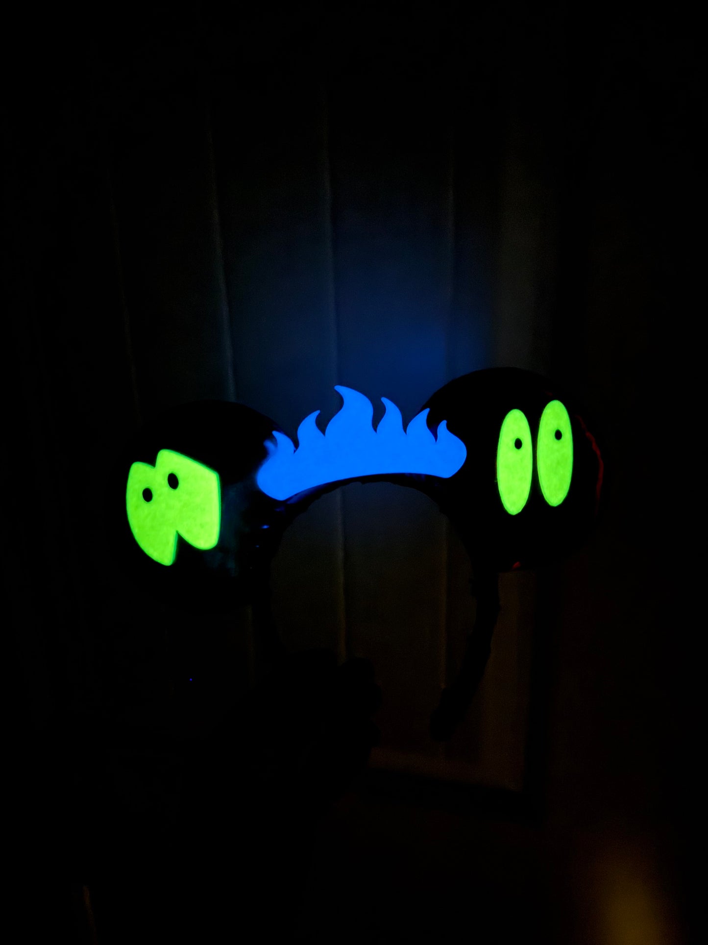 Glowing blue flames and green eyes on a dark background. This is the ears from the previous photo but showing that the eyes and flame are glow in the dark.