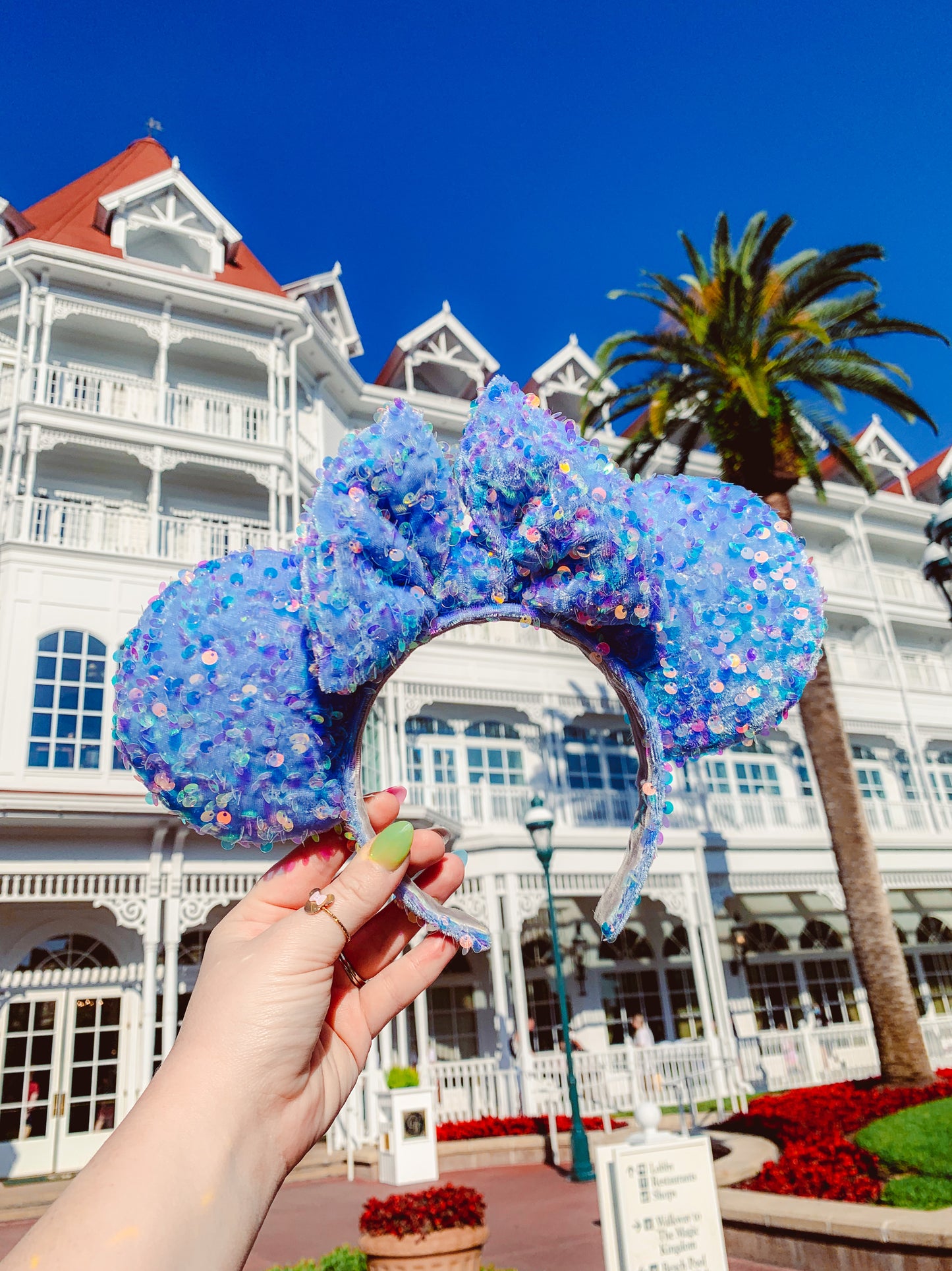 periwinkle mouse ears covered in iridescent sequins held in front of the Grand Floridian Resort