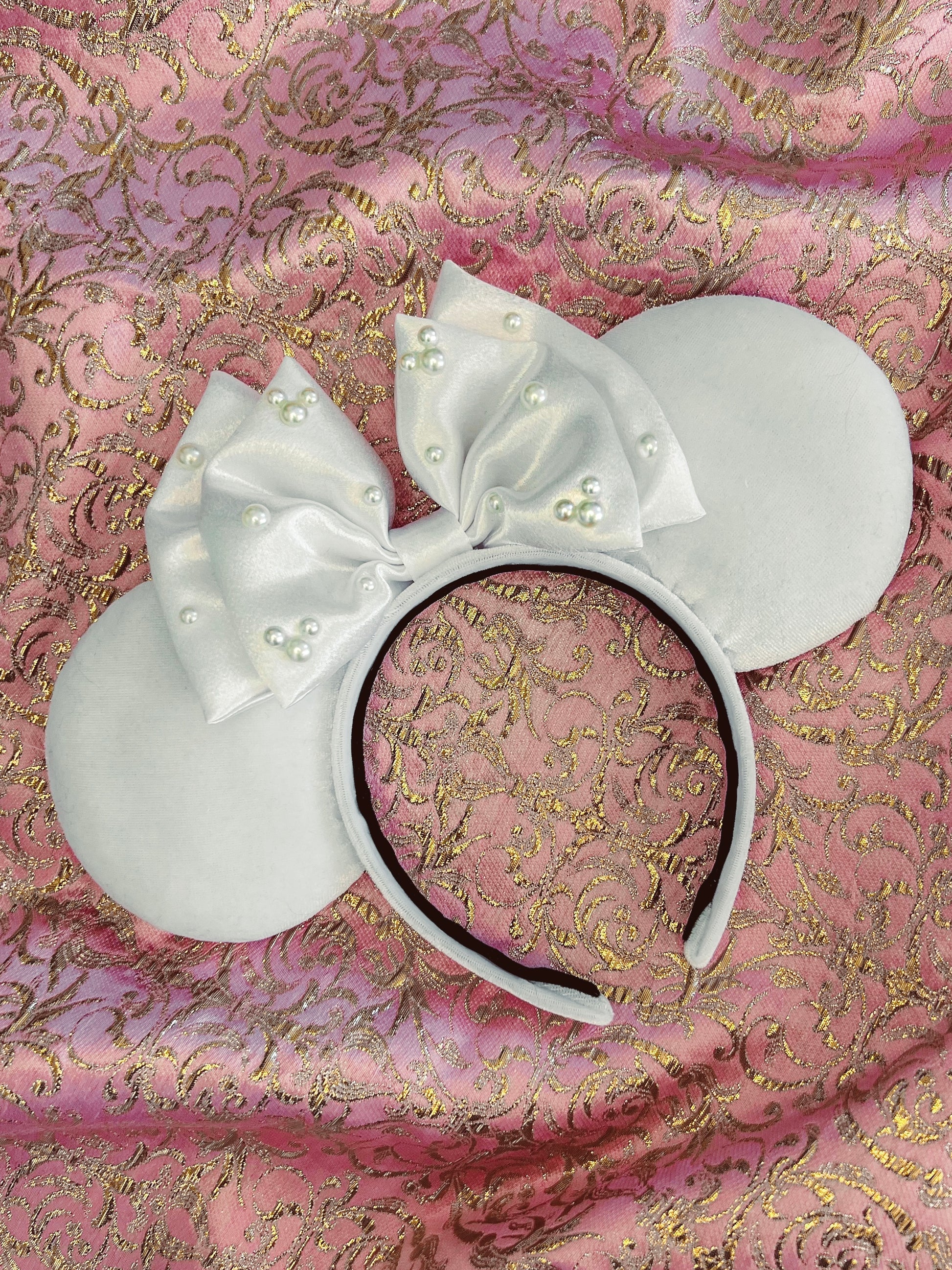 white velvet ears with a white satin bow with pearls on it laying on a pink background