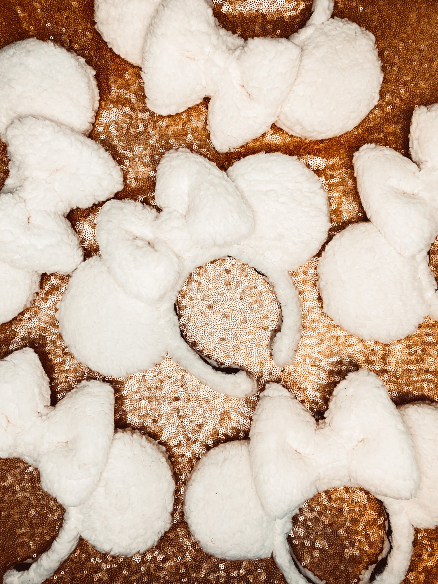 A collection of ivory sherpa ears laid out on a gold sequin surface.